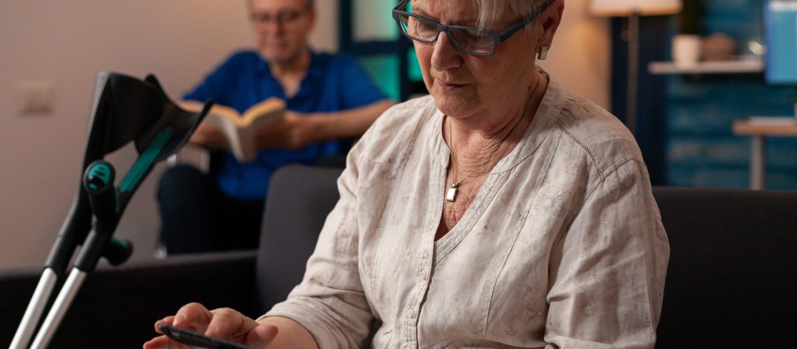 senior person with crutches looking at modern tablet